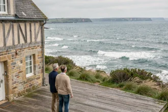 Couple devant une maison normande en pierre avec vue panoramique sur la mer de la Manche depuis la terrasse